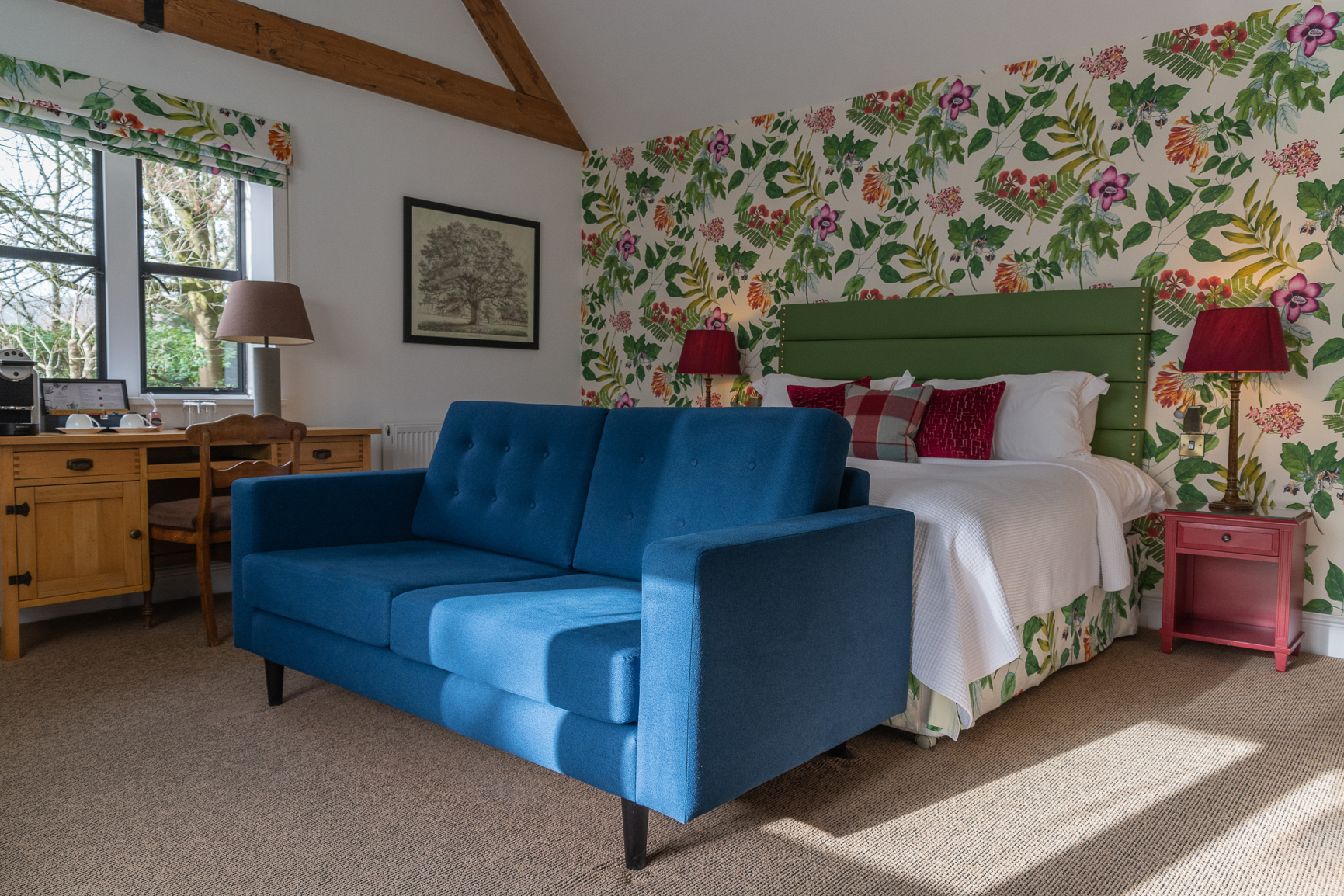 Garden room double bed at Baslow Hall, Derbyshire. Floral wallpaper behind the bed with Green headboard and Red bedside table lamps