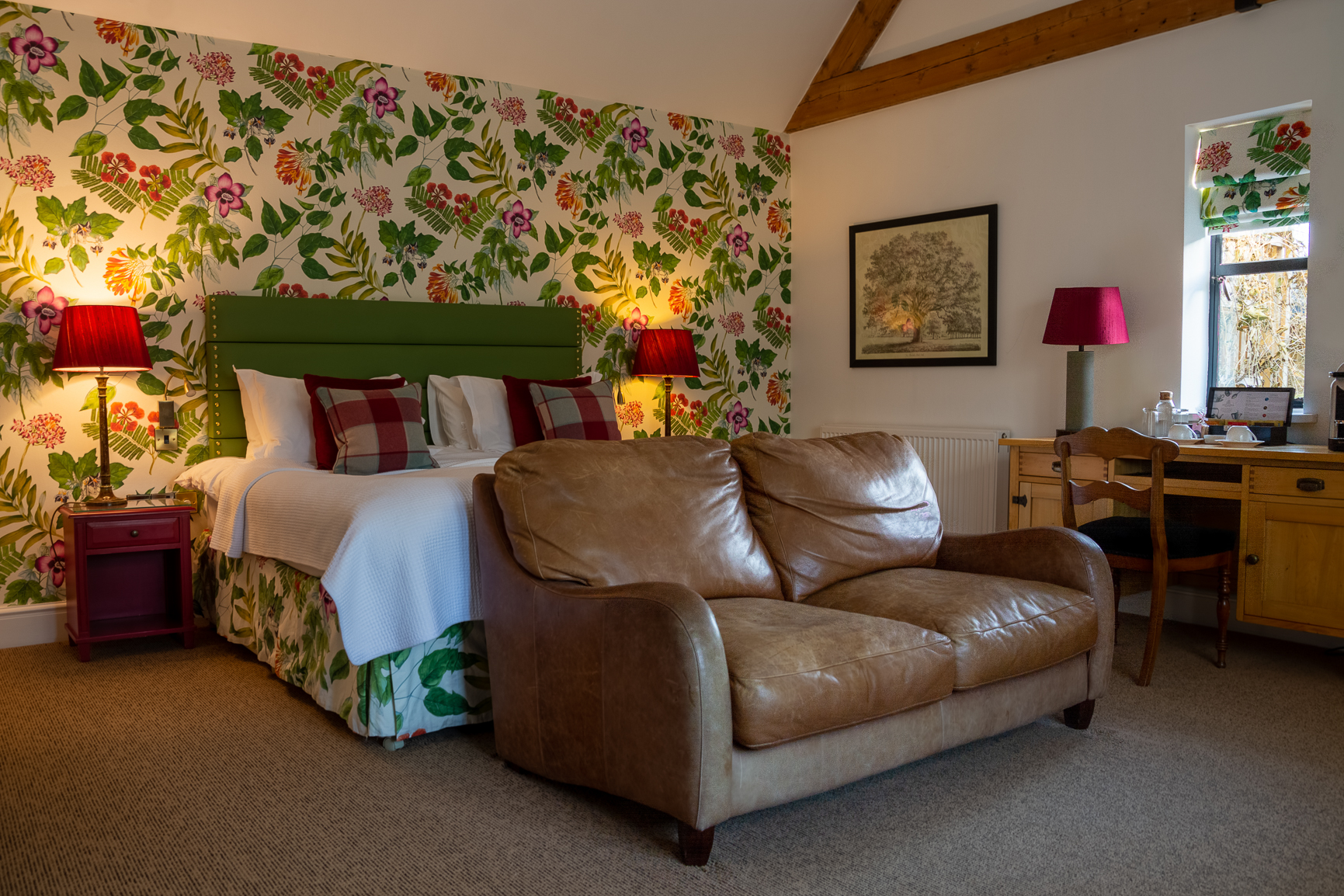 Garden room double bed at Baslow Hall, Derbyshire. Floral wallpaper behind the bed with Green headboard and Red bedside table lamps